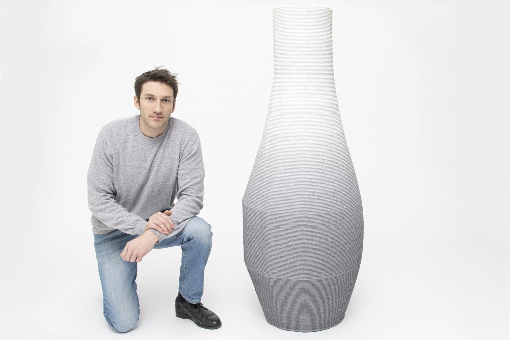 设计师Philipp Aduatz跪在他的3D打印渐变花瓶旁边。